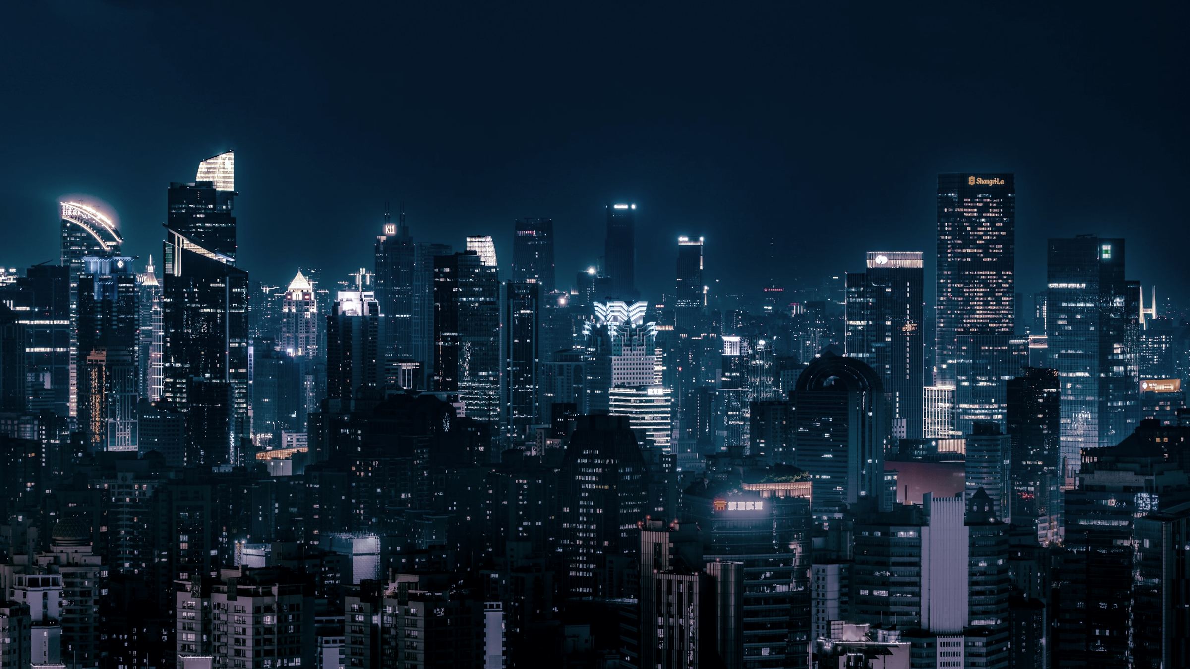 A dense city skyline at night, its towers lit against a deep blue sky