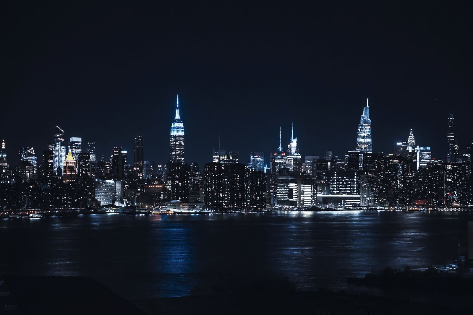 The Manhattan skyline at night, reflected in the river
